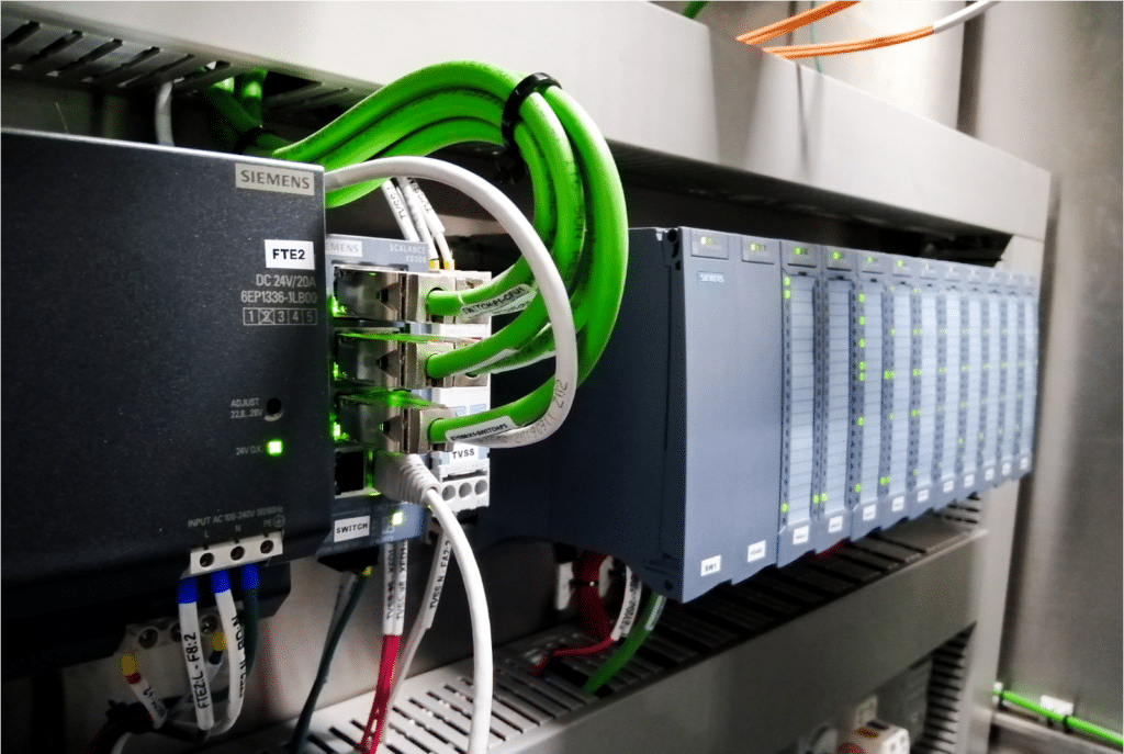 Server rack with Siemens PLC modules and green network cables in a data center environment.