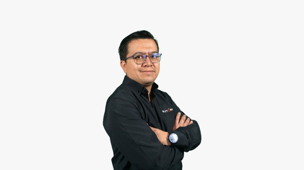 Portrait of a man with glasses and a black button-down shirt, arms crossed, against a light gray background, with a small logo on the chest.