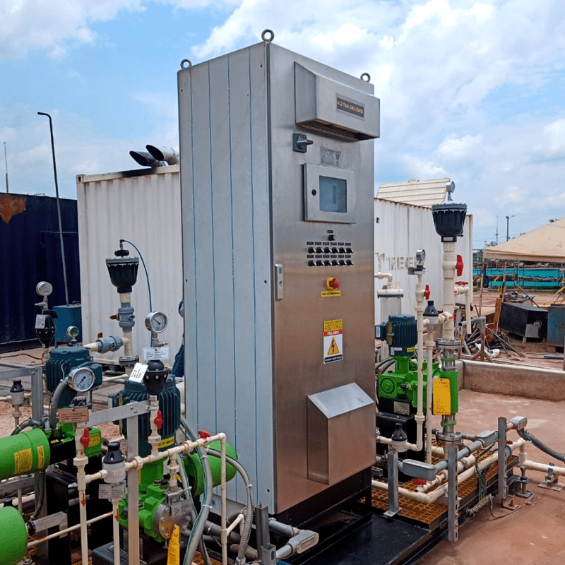 Industrial control cabinet with a touchscreen and rows of buttons, mounted beside green pumps and white piping outdoors.