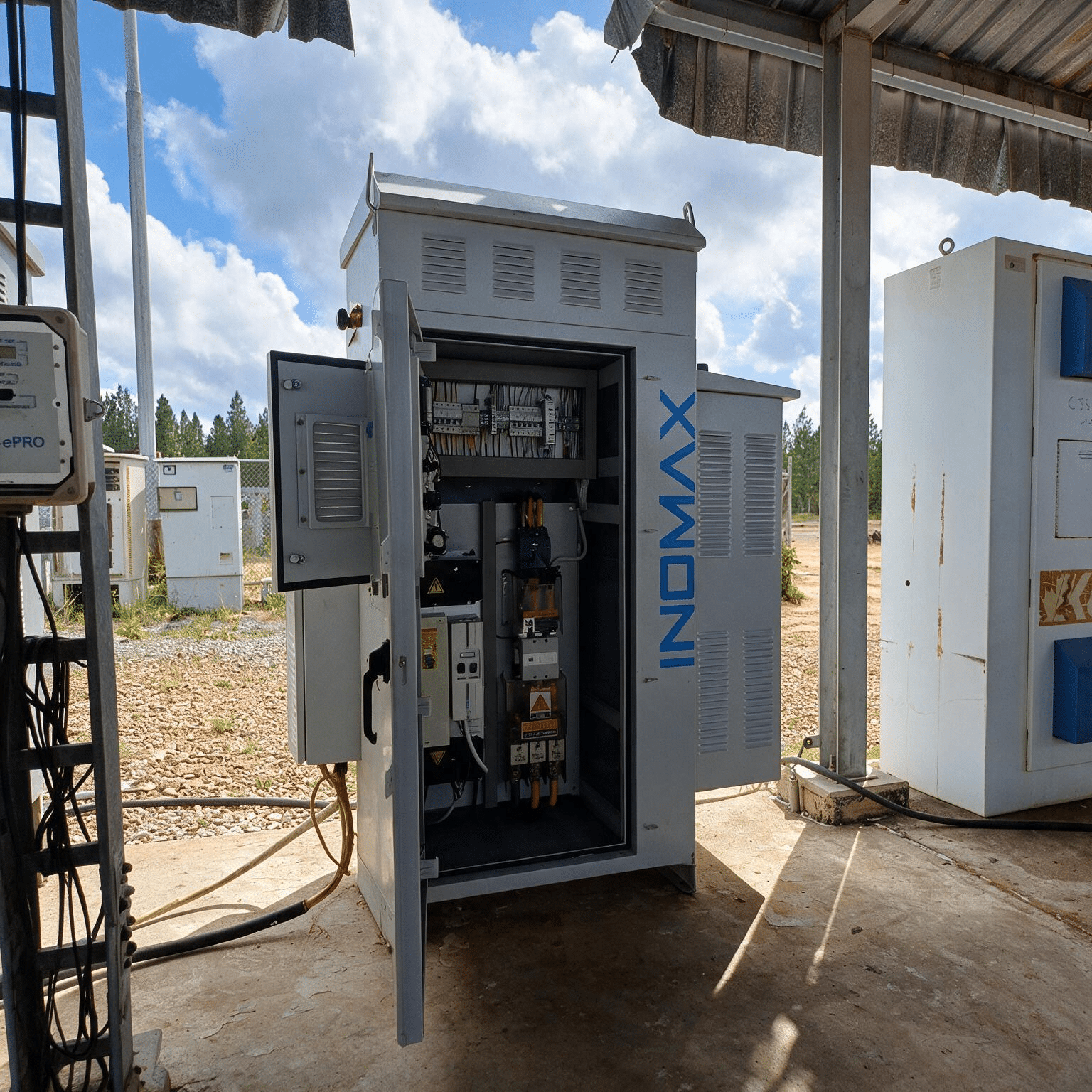 Open outdoor electrical control cabinet with exposed wiring and components under a shelter above.